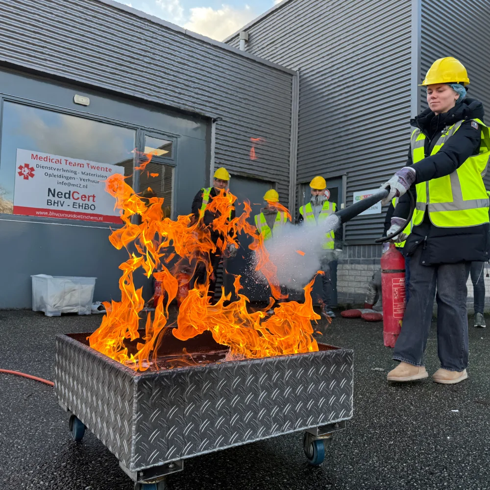 BHV-cursist blust een gecontroleerde brand tijdens een praktijktraining op de professionele buitenlocatie van NedCert Experts Doetinchem