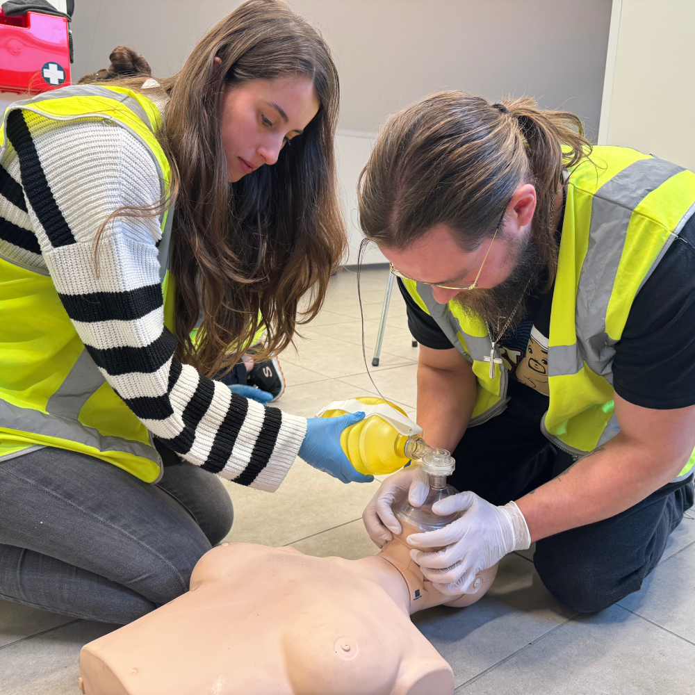 Twee deelnemers oefenen beademing met masker en beademingsballon op een reanimatiepop tijdens een BHV cursus in België