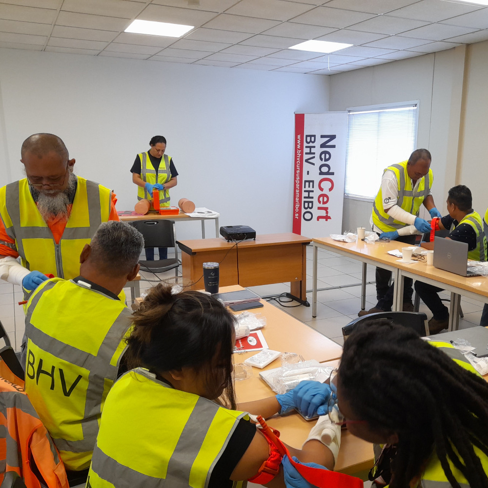 BHV-cursisten in Paramaribo oefenen het aanbrengen van verband en tourniquets tijdens een praktijkles in een ruime, goed ingerichte trainingszaal van NedCert Experts