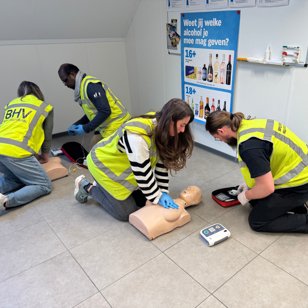 Vier cursisten oefenen gelijktijdig reanimatie met AED op oefenpoppen, terwijl de instructeur meekijkt.