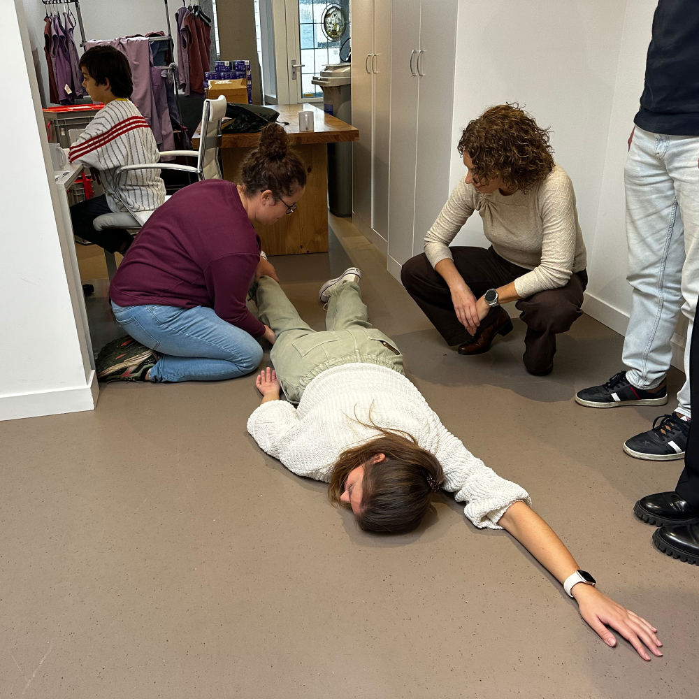 Twee cursisten benaderen een slachtoffer op de vloer van een smalle winkelruimte tijdens een incompany BHV-training.