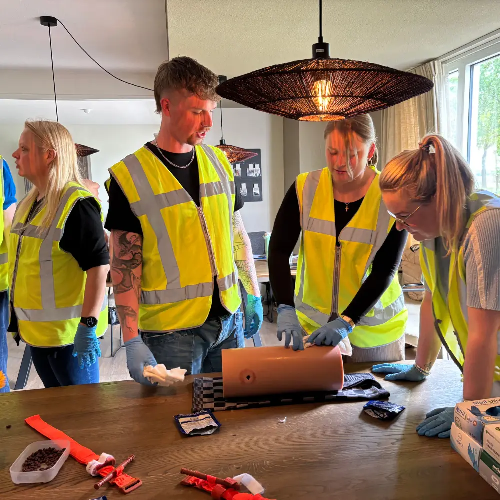 BHV-cursisten oefenen het stelpen van bloedingen op een dummy tijdens een incompany training in een woonkamer van een zorginstelling