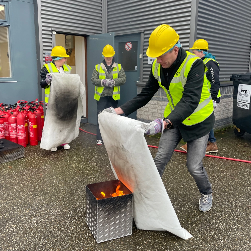 BHV-cursisten blussen een kleine brand met een blusdeken tijdens een training van NedCert Experts, ideaal voor brandveiligheid bij kleine bedrijven.