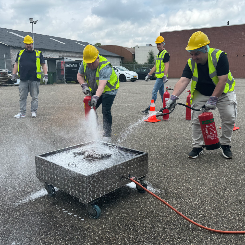 Cursist blust een oefenbrand met een brandblusser onder begeleiding van een instructeur tijdens een BHV-cursus