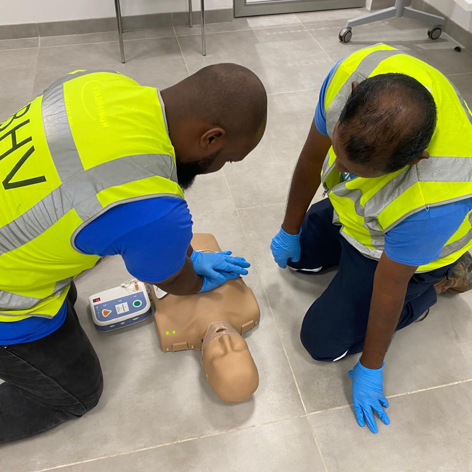 Twee cursisten oefenen borstcompressies op een reanimatiepop met een AED-trainer ernaast, tijdens een BHV-cursus van NedCert Experts in Paramaribo.