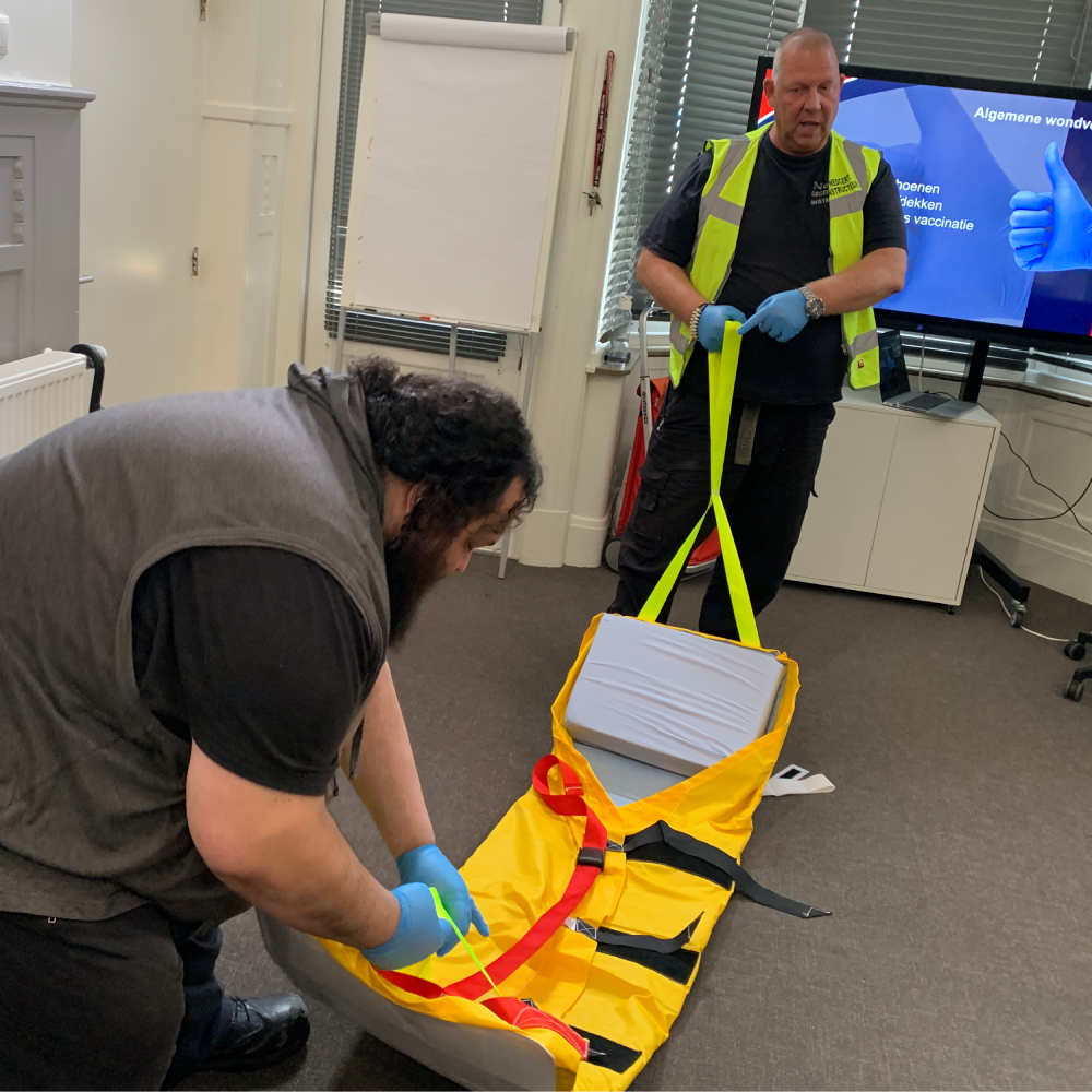Cursisten oefenen met een evacuatiematras tijdens een training van Cor Houet, voor het evacueren van iemand die niet zelfstandig naar buiten kan.