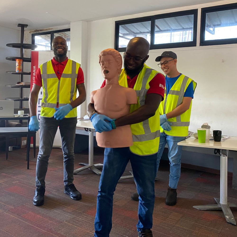 Cursist voert de Heimlich-manoeuvre uit op een oefenpop tijdens een BHV-cursus van NedCert Experts in Paramaribo, terwijl twee medecursisten toekijken.