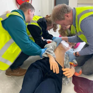 Cursisten brengen een chest seal aan op een "slachtoffer" tijdens een BHV-training van NedCert Experts, een cruciale vaardigheid voor traumakit-gebruik in bedrijven.