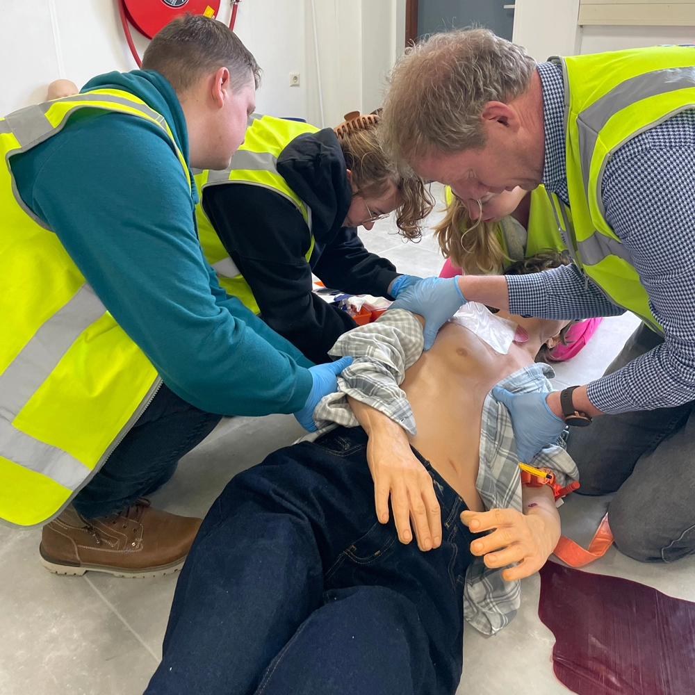 Cursisten brengen een chest seal aan op een "slachtoffer" tijdens een BHV-training van NedCert Experts, een cruciale vaardigheid voor traumakit-gebruik in bedrijven.