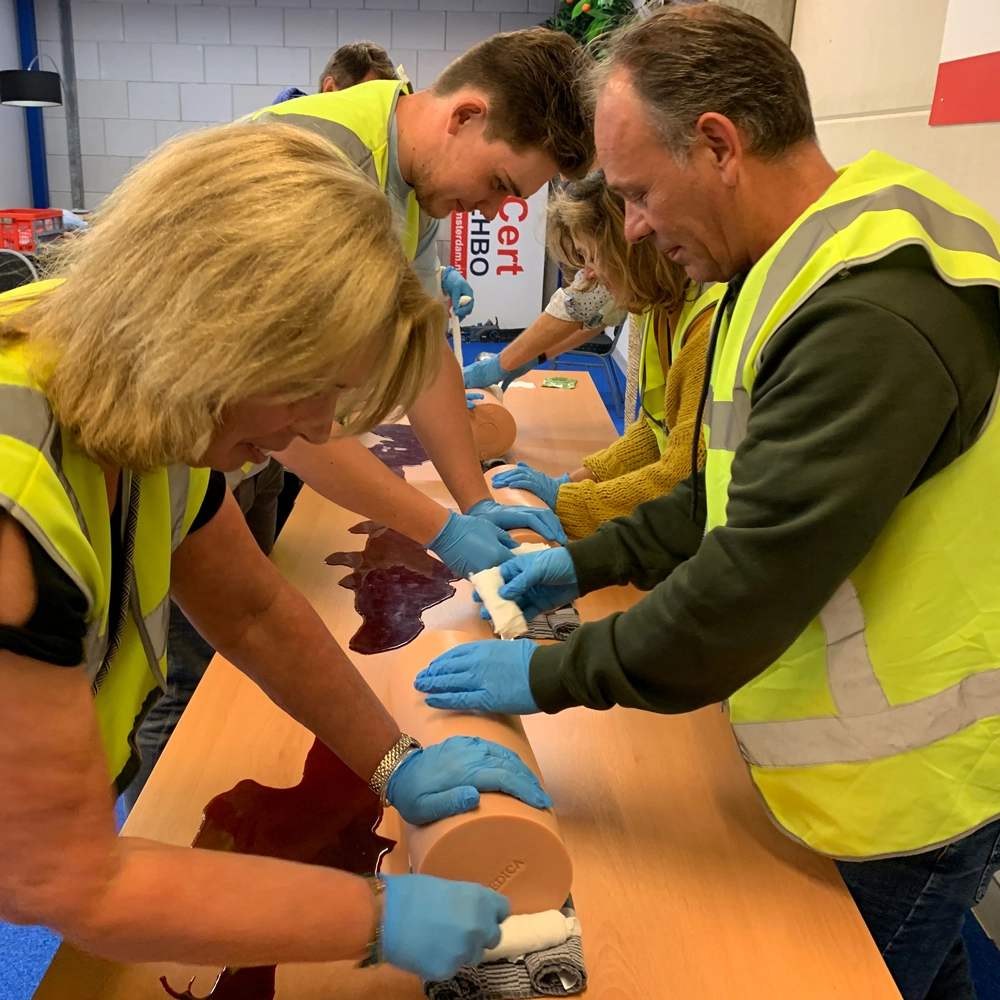 Cursisten oefenen met hemostatisch gaas op een oefenarm tijdens een BHV-training van NedCert Experts, een belangrijke vaardigheid voor traumakit-gebruik in bedrijven.