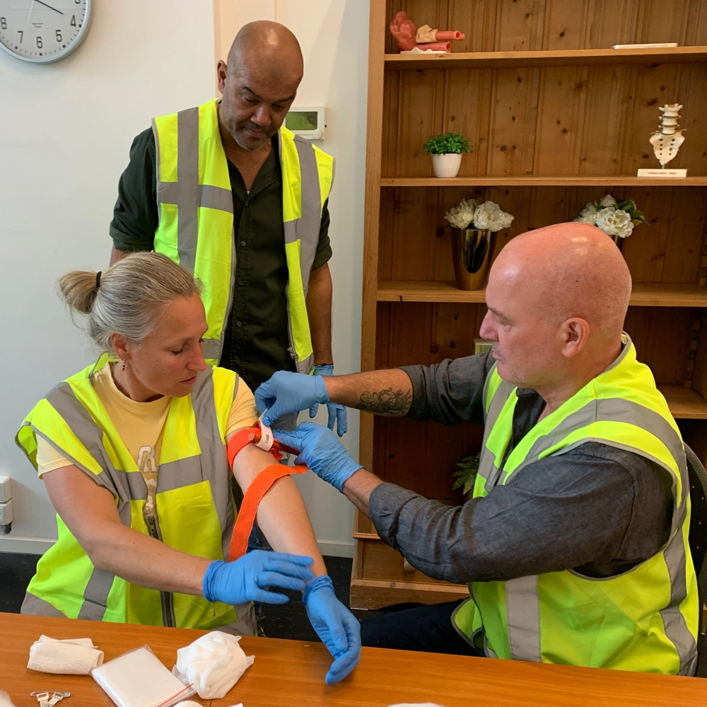Cursisten brengen een tourniquet aan tijdens een BHV-training van NedCert Experts, een belangrijke vaardigheid voor traumakit-gebruik in bedrijven.