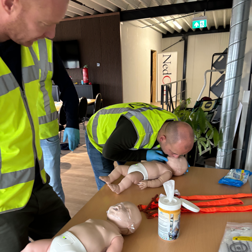 Cursist beademt een babyreanimatiepop mond-op-mond-en-neus tijdens een SEHSO-cursus van NedCert Experts in Emmen, terwijl de instructeur meekijkt.